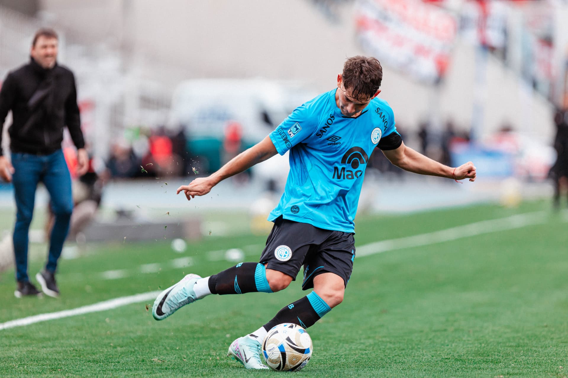 Jugador de Belgrano ejecutando un pase largo al costado de la cancha