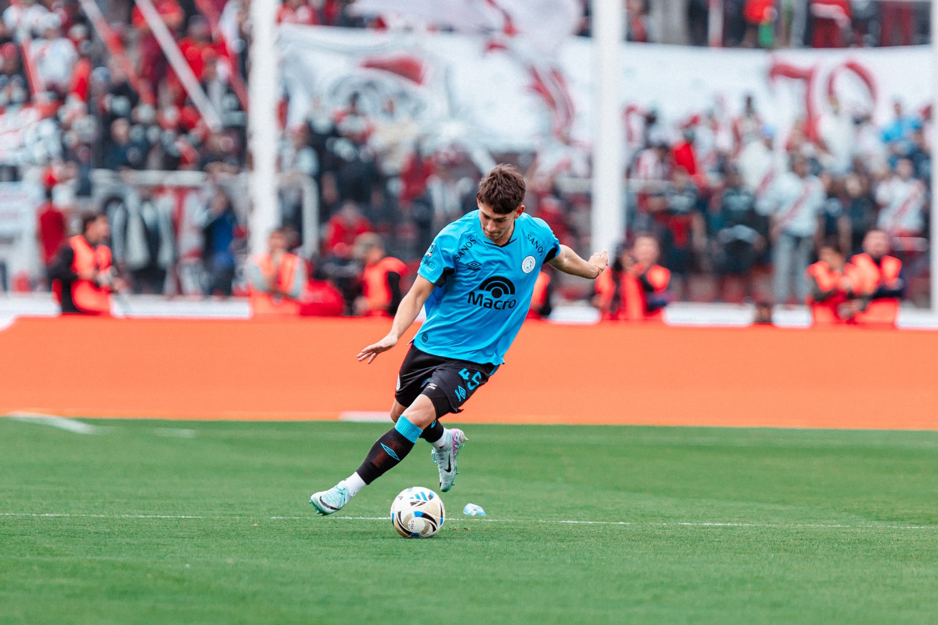 Jugador de Belgrano conduciendo la pelota frente a una tribuna colmada