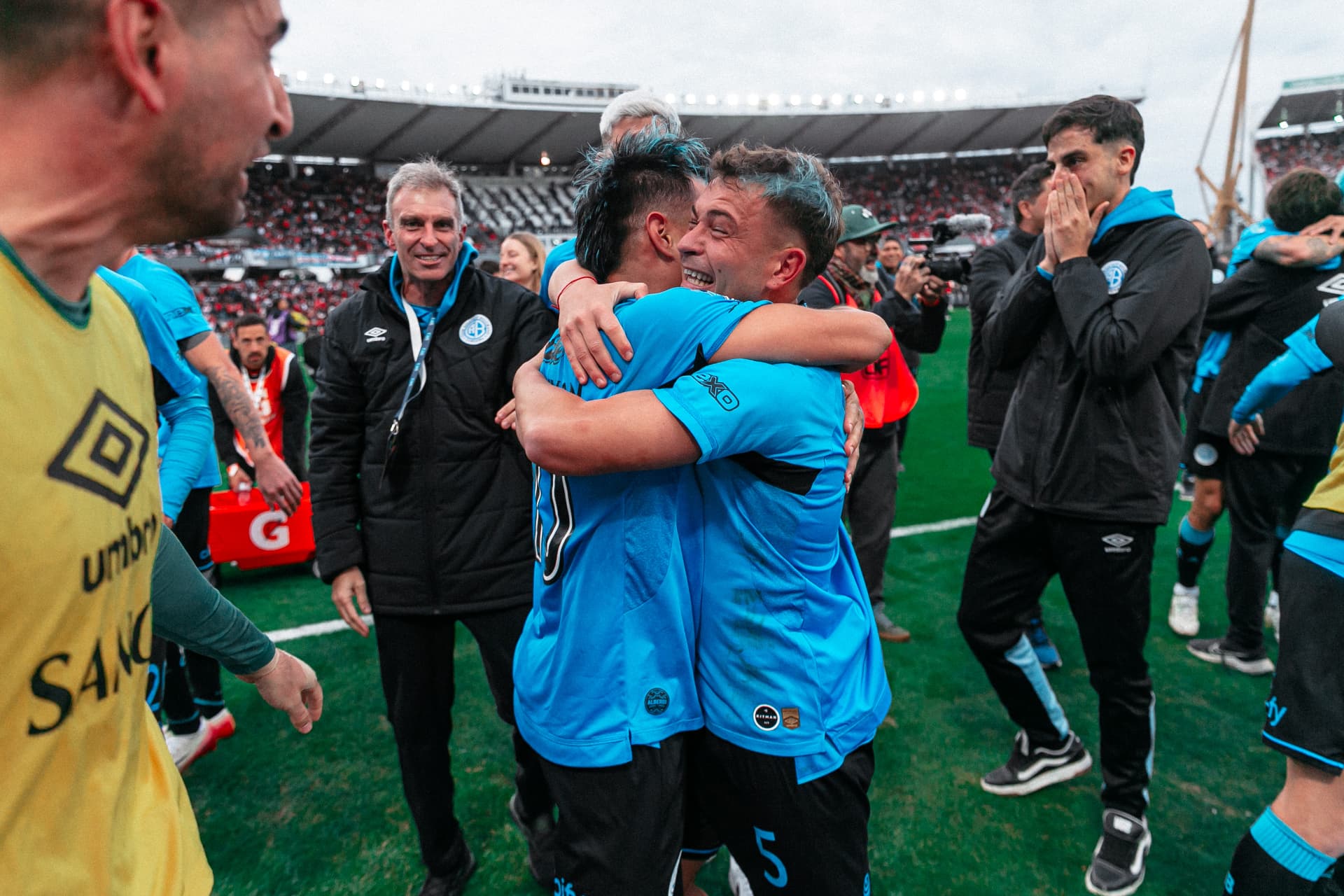 Dos jugadores de Belgrano abrazados, el cuerpo técnico se acerca